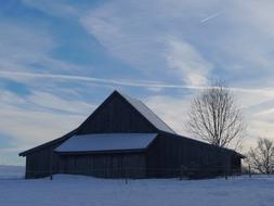 Beautiful, snowy landscape with the hut and trees, under the blue sky with clouds, in the winter