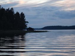 Beautiful landscape of the lake with ripple, among the trees, in Finland, at colorful sunset with clouds