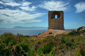 Beautiful and colorful Mediterranean coast with colorful plants and watchtower, at background with mountains