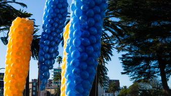 Shiny, blue and orange balloons near the buildings, among the trees, in sunlight