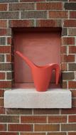 Shiny, orange watering can on the ledge of the brick wall