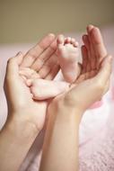 Mother holding cute baby legs in the hands, in light