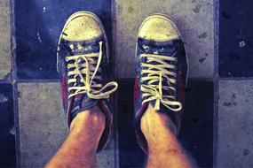 Top view of the person in dirty, old slippers on the black and white tiles