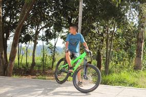 Boy cycling on the green BMX bike, on the road, among the plants