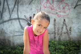 Portrait of the cute girl child among the green plants, near the wall with colorful drawings