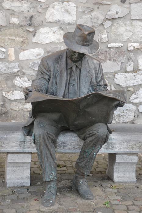 sculpture of a man sitting on a bench with a book in his hands