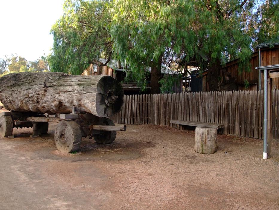 Old cart with the tree log, near the fence and colorful trees