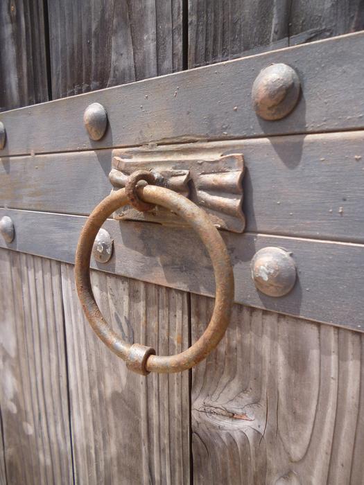 Close-up of the metal knocker on the wooden gate, in light