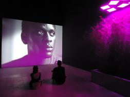 People looking on the screen in the building with purple lights, at Biennale, in Venice, Italy
