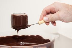 Holding beautiful pastry in the melted chocolate, above the bowl