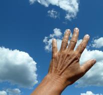 Close-up of the person's raised hand, under the blue sky with clouds