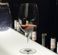 Close-up of the shiny wine glass with red wine on the table in light, near the colorful bottles