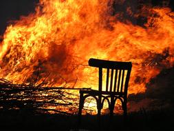 Silhouette of the chair, near the wood and colorful fire, among the darkness, at the night