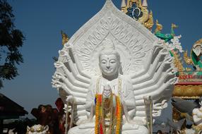 Beautiful, white statue of Buddha with 18 arms, near the colorful temple