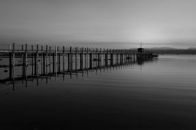 Black and white photo of the river with the pier, with reflections, under the clouds