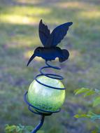 Green and yellow ball decoration with beautiful, blue hummingbird, among the colorful plants