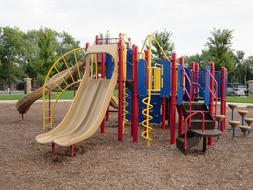 Beautiful landscape with the colorful playground near the plants, under the clouds