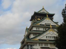 Beautiful Osaka Castle with gold details, near the trees, in Japan, under the blue sky with clouds