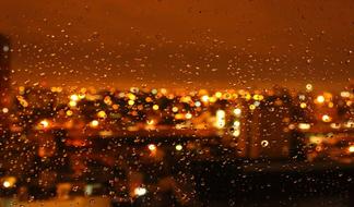 Beautiful landscape with colorful lights, behind the window with water drops