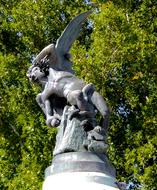 Shiny sculpture of Lucifer, in sunlight, near the green plants