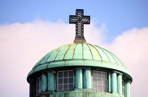 Green roof of the old tower, with cross, under the blue sky with clouds
