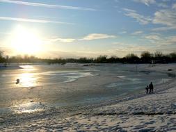 People near the beautiful frozen lake, on landscape, at colorful and beautiful sunset