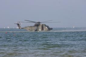 military helicopter in flight over water