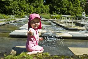 Cute child in pink cap, swimming in the fountain, among the plants