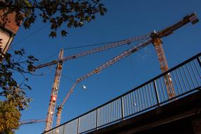 Bridge and cranes, near the colorful trees and buildings, under the blue sky