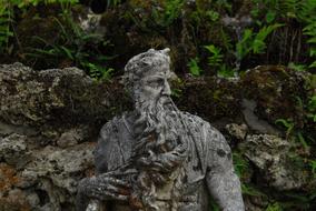 Beautiful stone figure of the man with beard, in the garden with plants