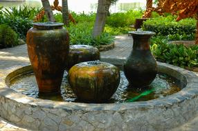 Beautiful and colorful fountain with vases, among the colorful plants