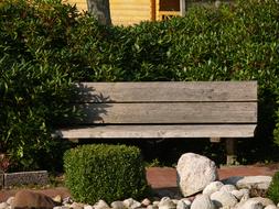 Beautiful, wooden bench among the plants and stones, in sunlight