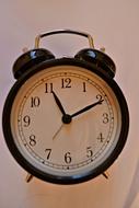 Close-up of the shiny, black and metallic clock, at background with the wall