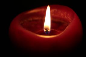 Close-up of the burning, red candle with light, among the darkness, at the Christmas