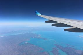 View of the flying plane's wing above the colorful landscape with water