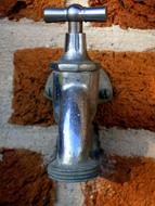 Close-up of the shiny metal faucet in the brick wall