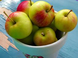 Colorful, shiny apples in the pot with images, on the blue, wooden surface