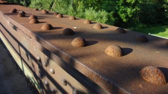 Close-up of the rusty bridge railing in sunlight and shadows, near the green plants