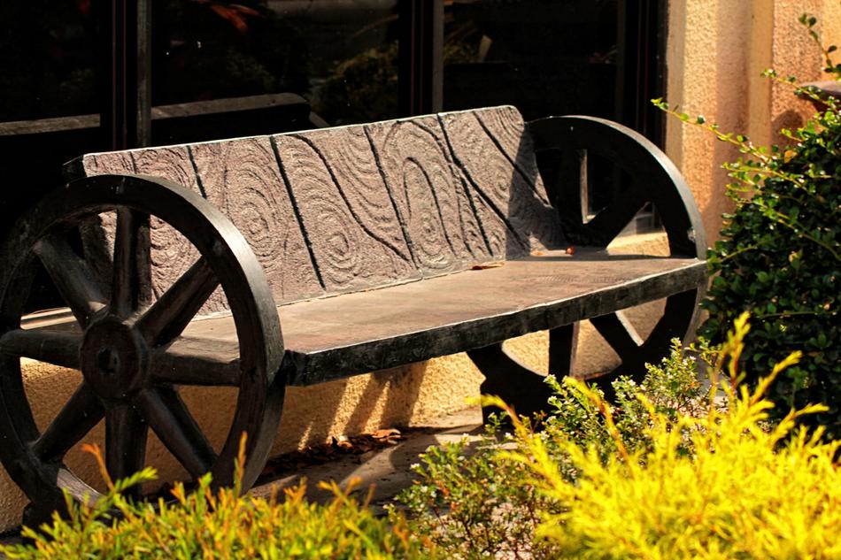 Beautiful, brown, wooden bench with patterns and wheels, among the colorful plants