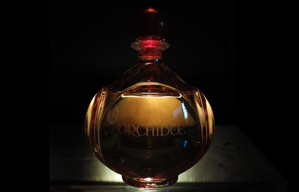 Close-of the beautiful and colorful, shiny perfume bottle at backlight, among the darkness