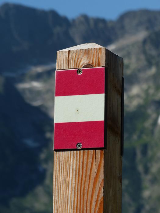 Wooden pole signpost with red and white mark, near the beautiful mountains