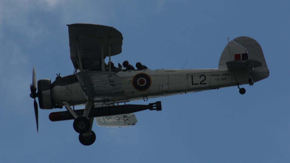 People in the flying Swordfish Navy plane with bomb, under the blue sky with clouds