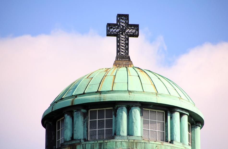 Green roof of the old tower, with cross, under the blue sky with clouds
