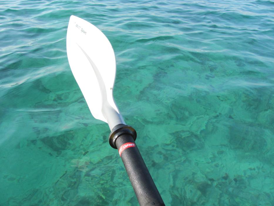 Close-up of the white boat paddle, above the colorful water with ripple, in Salento, Italy