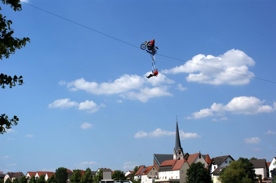 Landscape with the acrobats with the motorbike, on the high ropes, near the colorful buildings and plants