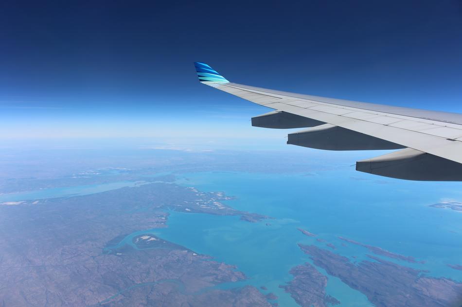 View of the flying plane's wing above the colorful landscape with water