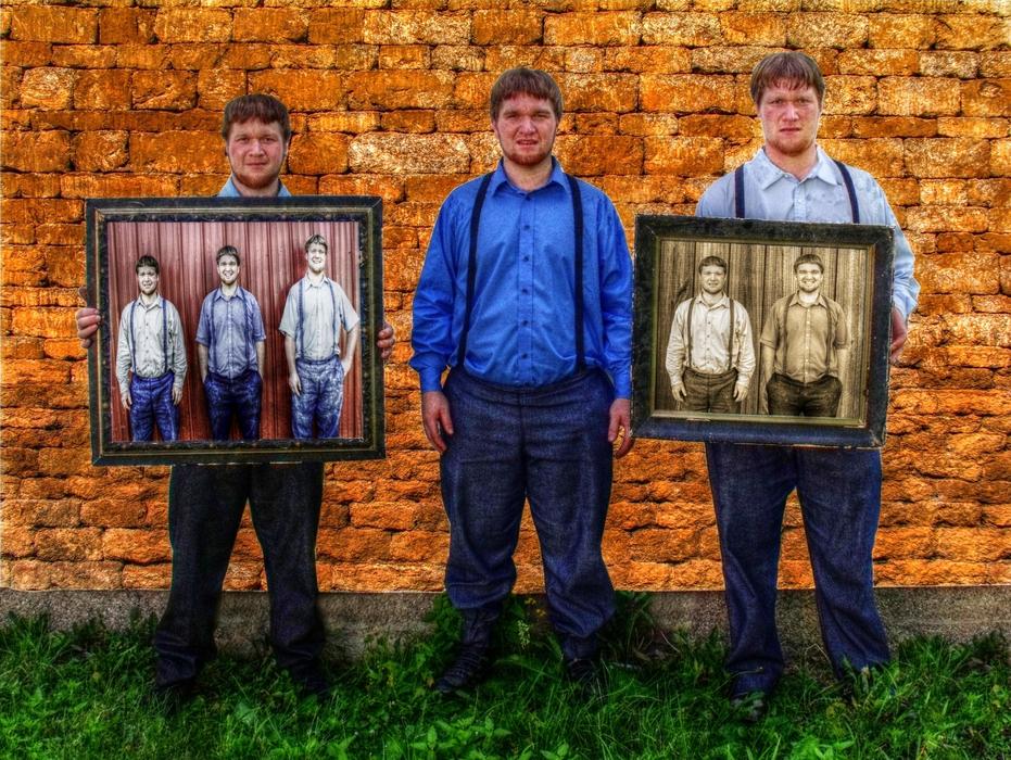 three young men with framed pictures at brick wall