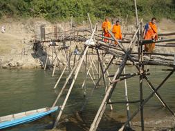 three Buddhist Monks walking on wooden bridge over river, Laos