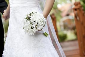 Bride in the beautiful, patterned wedding dress, with the beautiful, white bouquet with the flowers