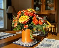 Close-up of the beautiful, shiny, orange pot with colorful flowers, on the table, among the furniture